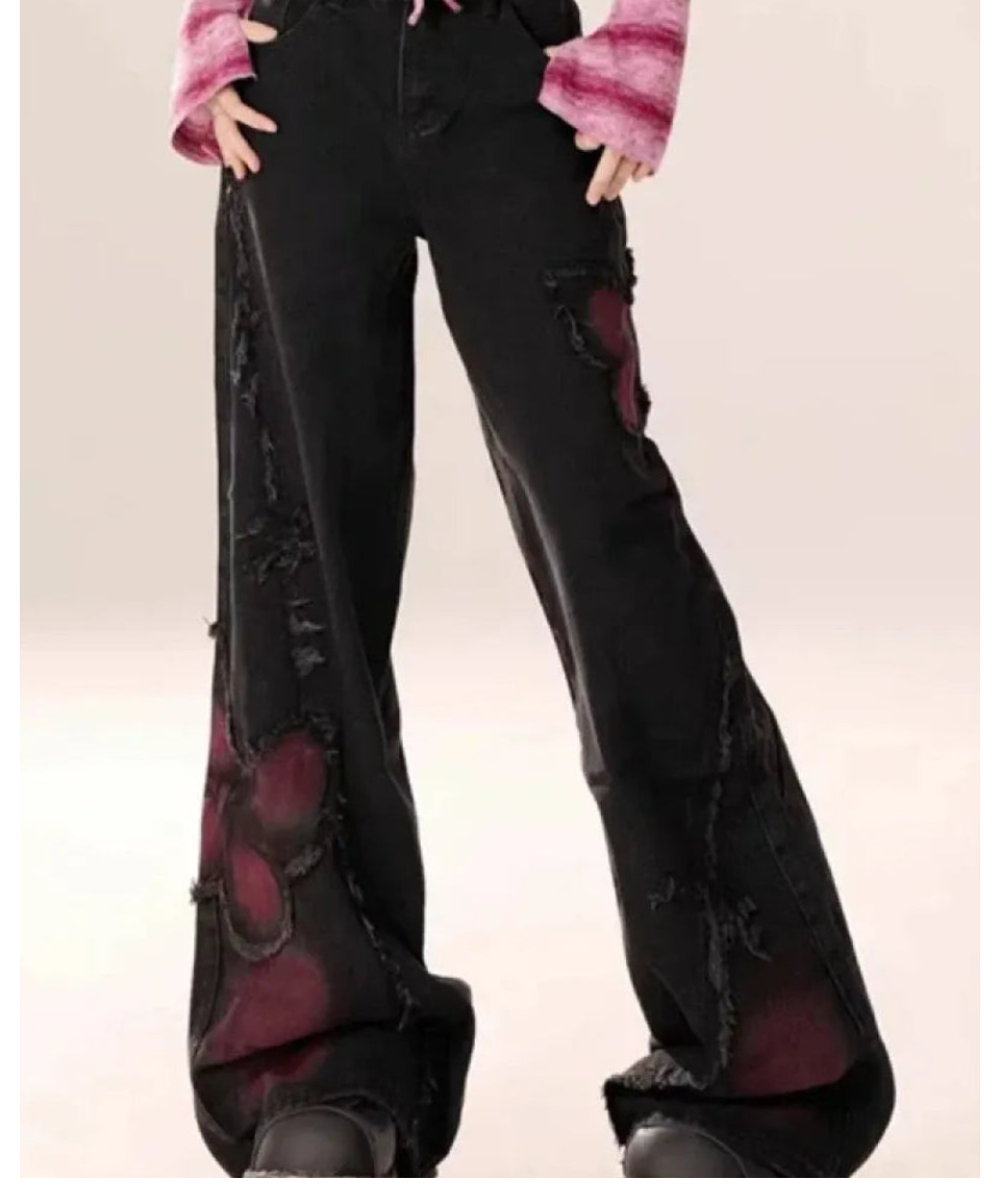 Black flared pants with red heart designs worn by a person on a white background